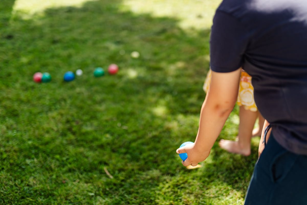 Person throwing a bocce ball on a green lawn